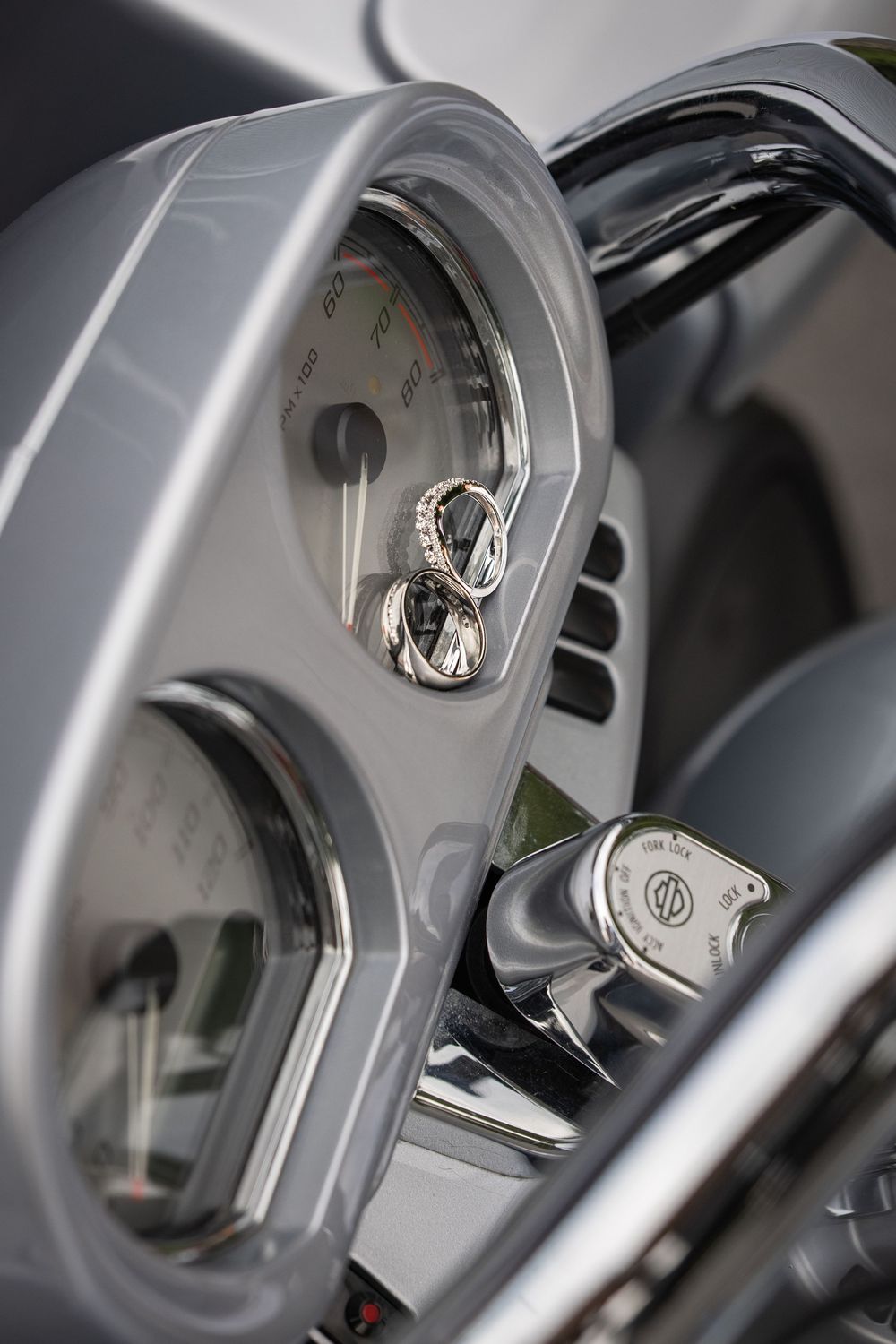 Wedding rings resting on a motorcycle dashboard speedometer, chrome details gleaming on a Harley-Davidson instrument cluster.