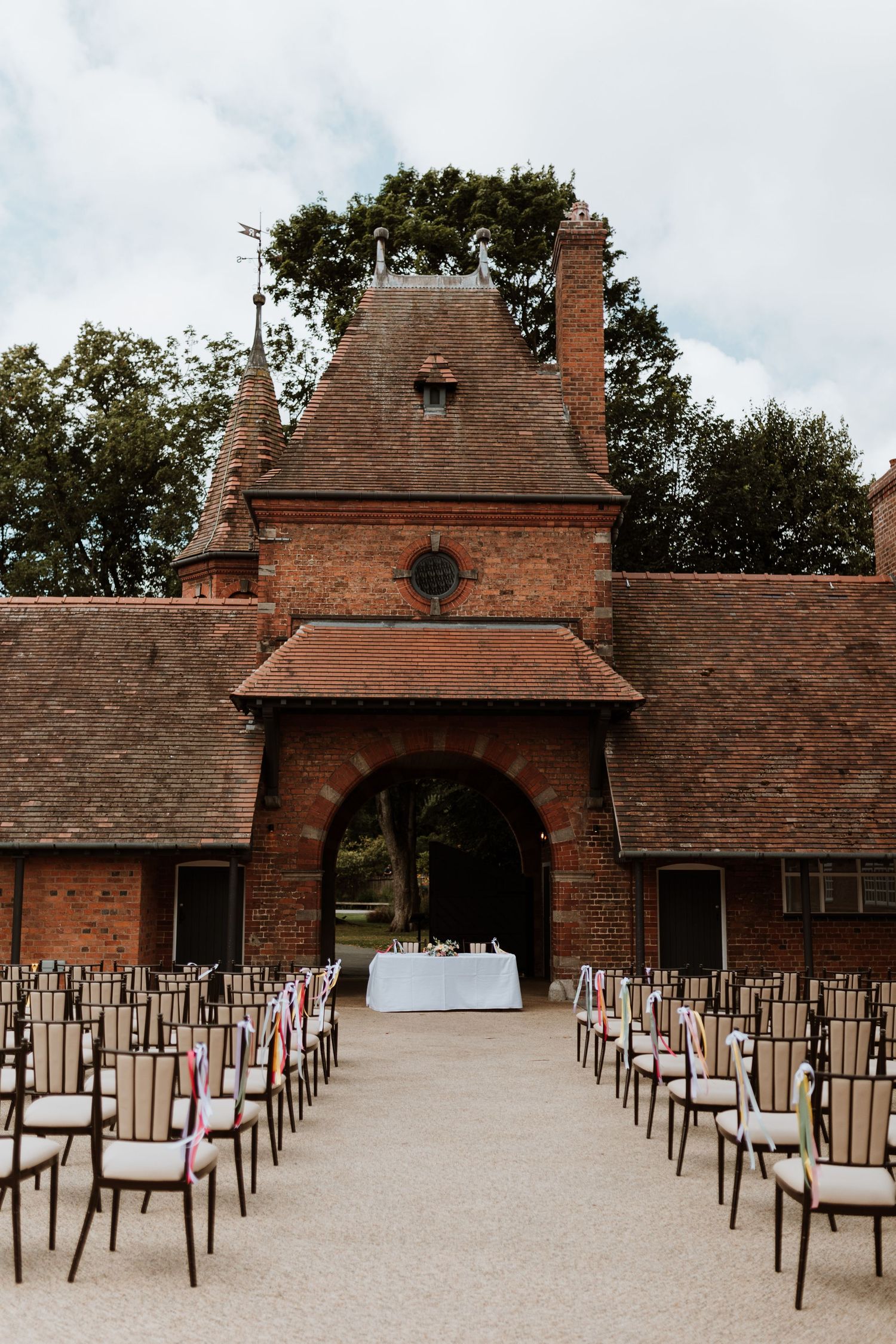 Outdoor wedding ceremony setup with rows of chairs leading to a brick archway entrance at an elegant historic venue.