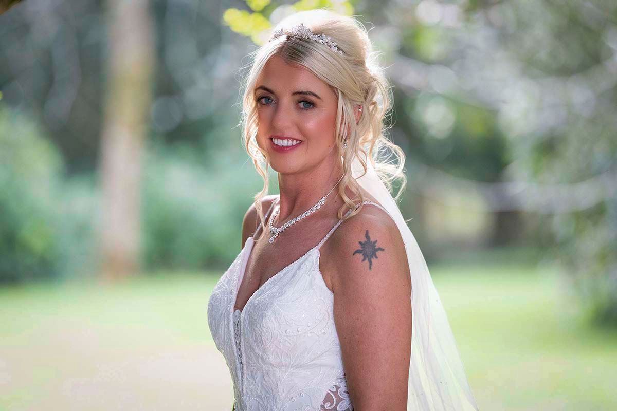 Smiling bride in white lace gown with veil, pearl necklace pose at Armathwaite Hall Hotel in the Lake District