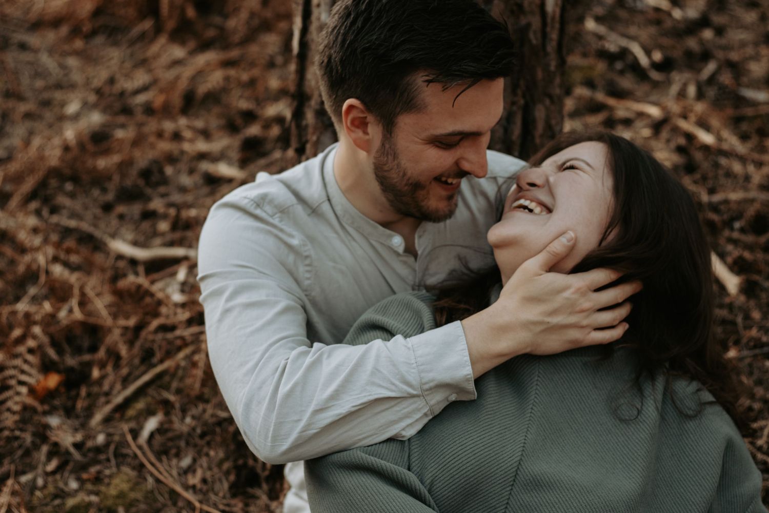 A couple laughing and embracing tenderly in an autumn forest setting, sharing a romantic moment outdoors.