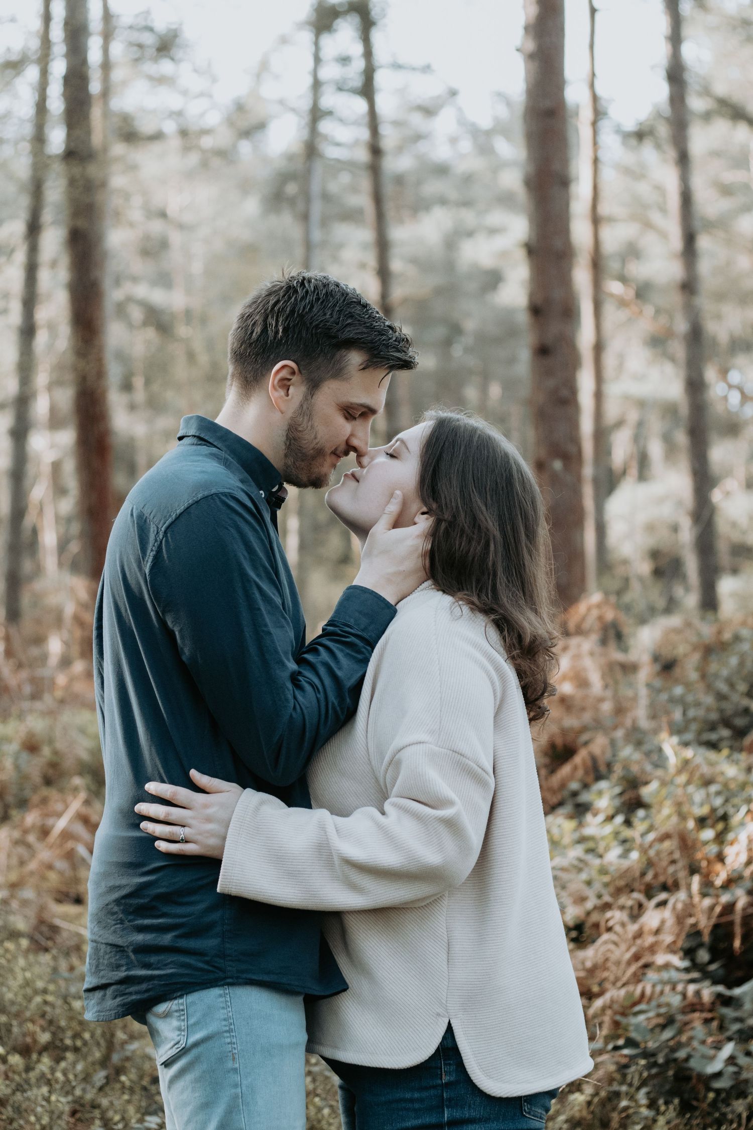 Couple sharing a romantic kiss in a forest setting, man tenderly holding womans face.