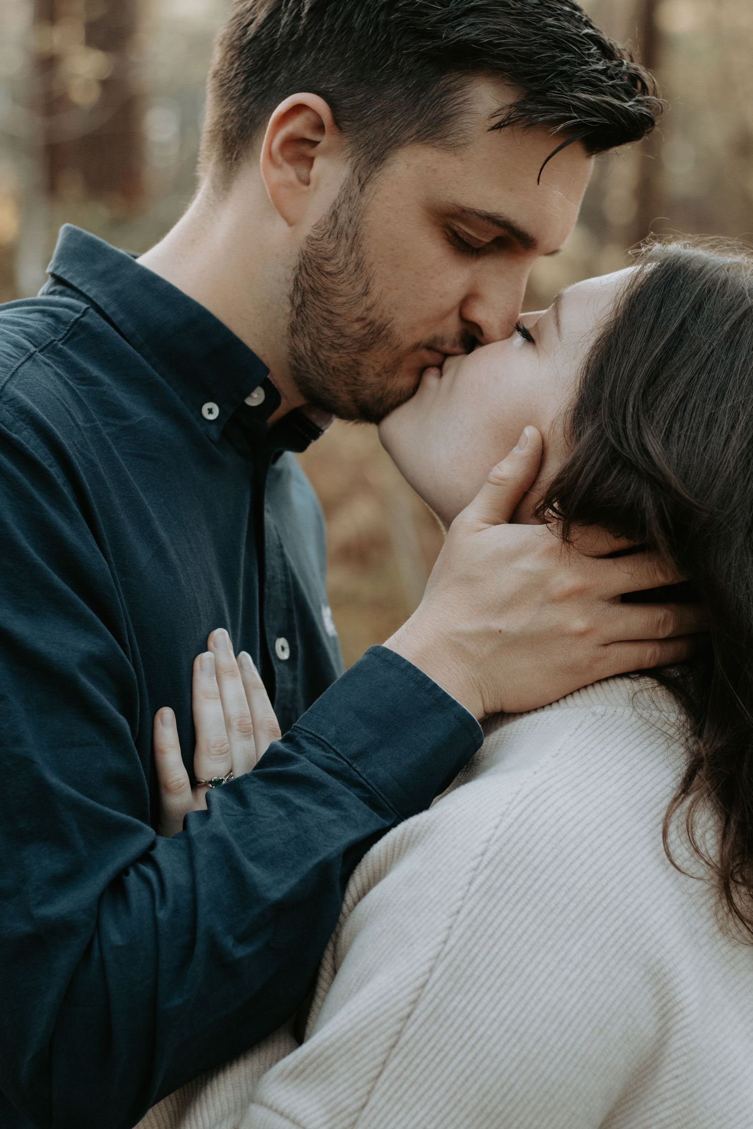 Close-up of a couple kissing outdoors, man gently cupping womans face in woodland.