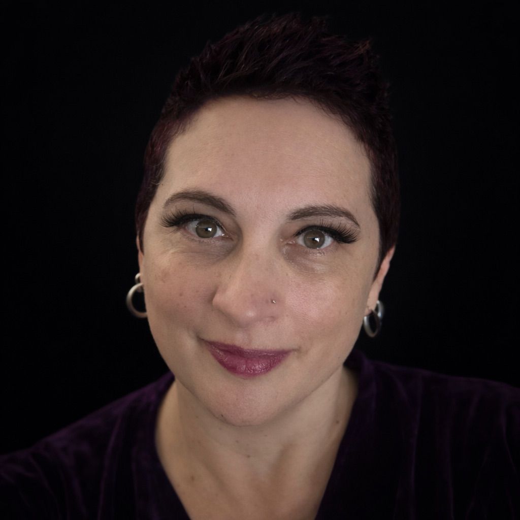 Woman with short dark hair, hoop earrings, and purple lipstick smiling against a black background.