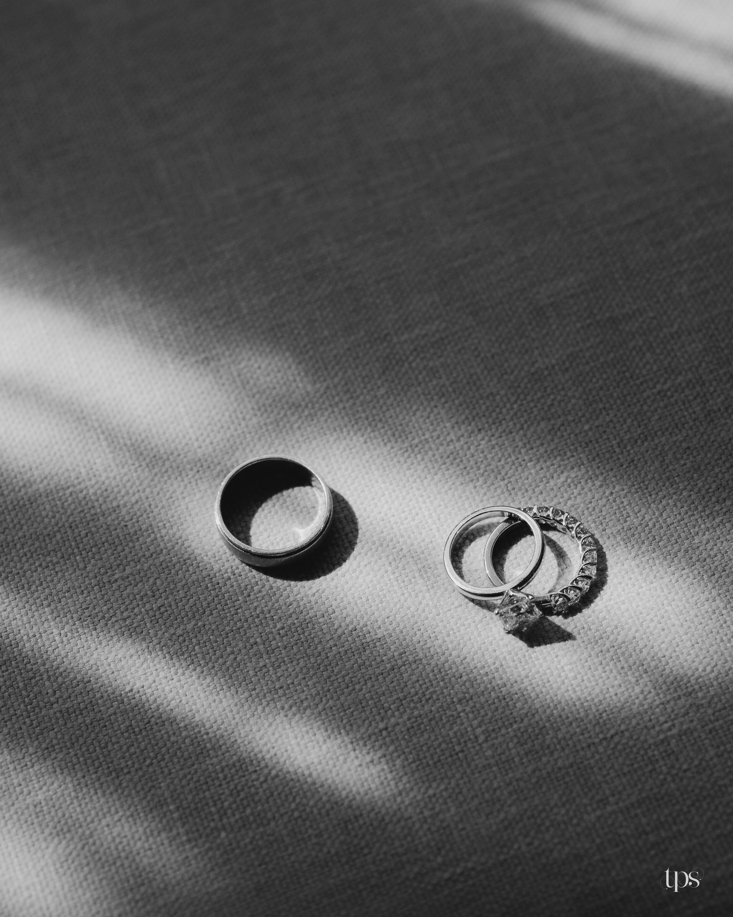 Black and white photo of a mens wedding band and diamond engagement ring set on a textured fabric surface.