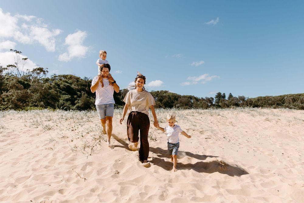 Happy family with two young children running on a sunny sandy beach with blue sky.