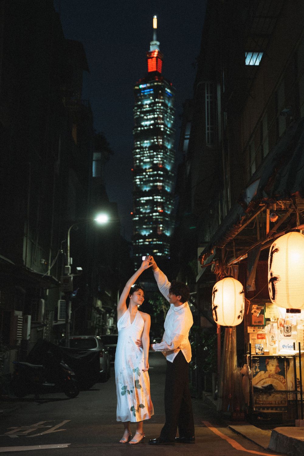 Couple dancing on a Taipei street at night with Taipei 101 skyscraper glowing in the background.
