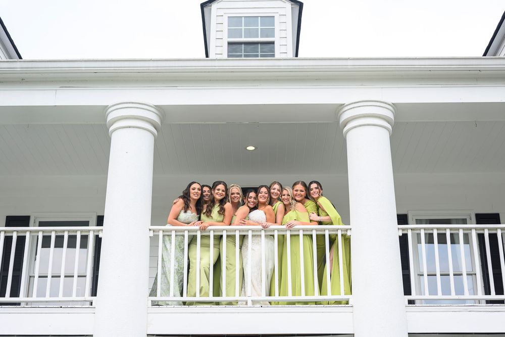 Bridesmaids in lime green dresses posing with bride on white colonial balcony with pillars at wedding venue.