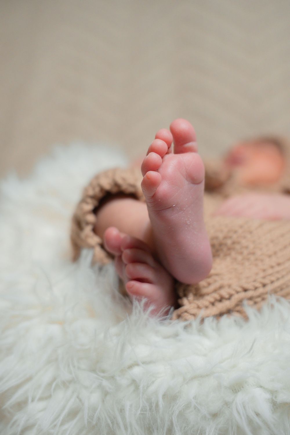 Newborn baby yawning in a cozy brown crocheted bear hat and outfit, resting on a fluffy white blanket.