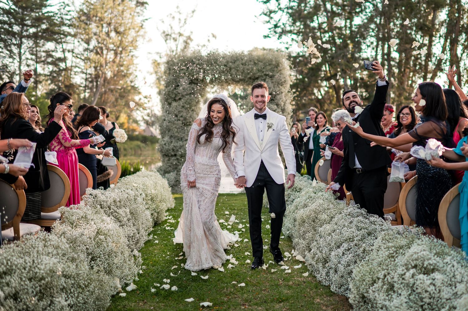 Wedding guests gather outdoors surrounded by white baby's breath flowers and greenery for a romantic ceremony.