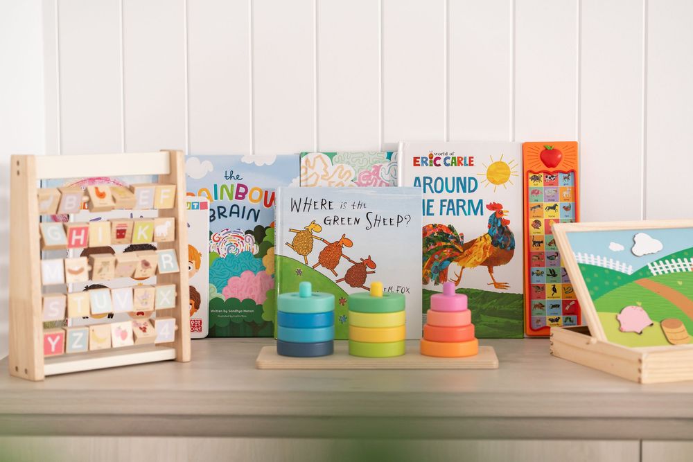Colorful children's books and wooden educational toys displayed on a shelf, including stacking rings and an alphabet board.