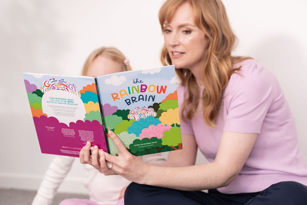 A mother and young daughter sit together reading The Rainbow Brain colorful children\u2019s book about neurodiversity.