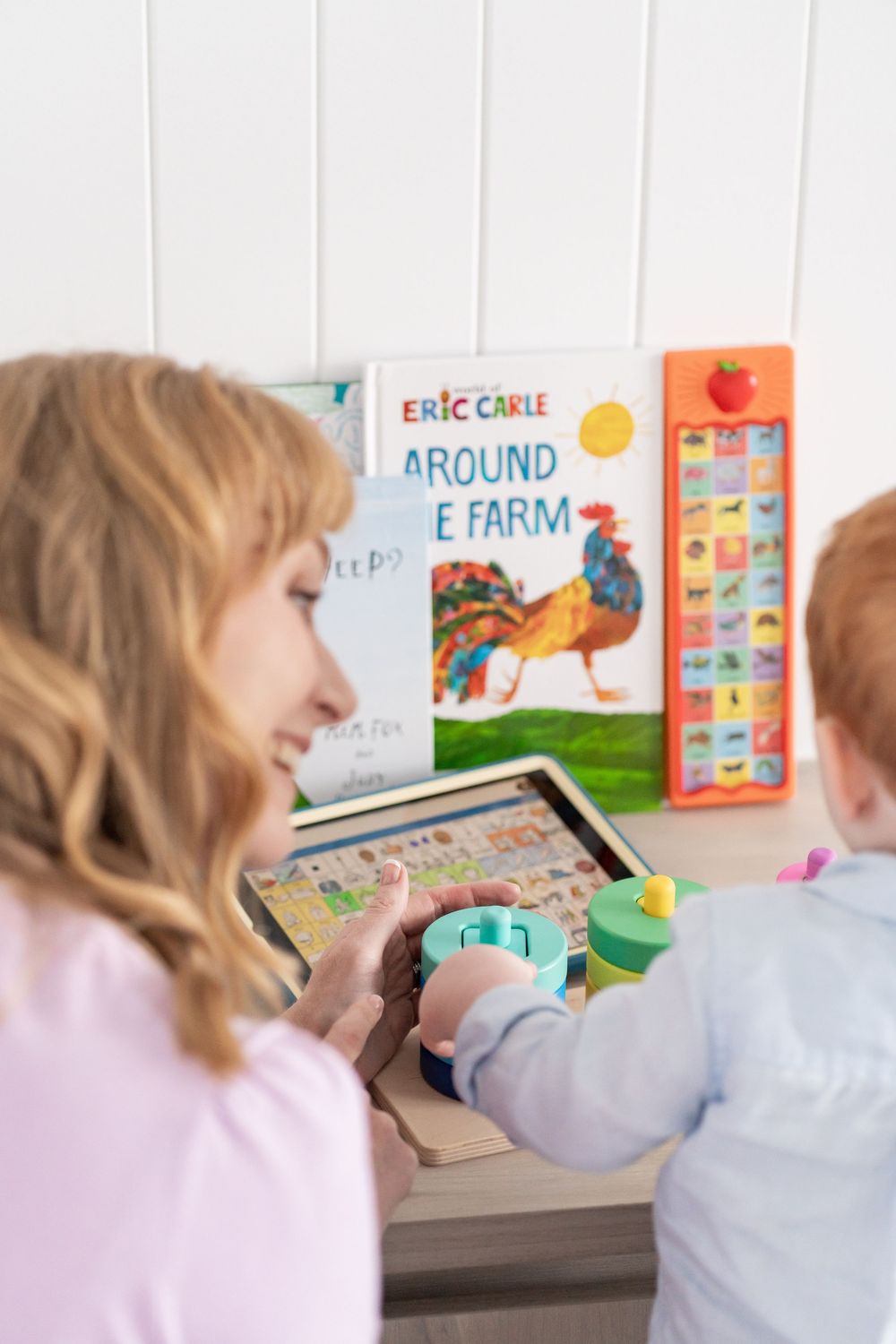 Woman and toddler playing with wooden alphabet puzzle board beside Eric Carle Around the Farm book.