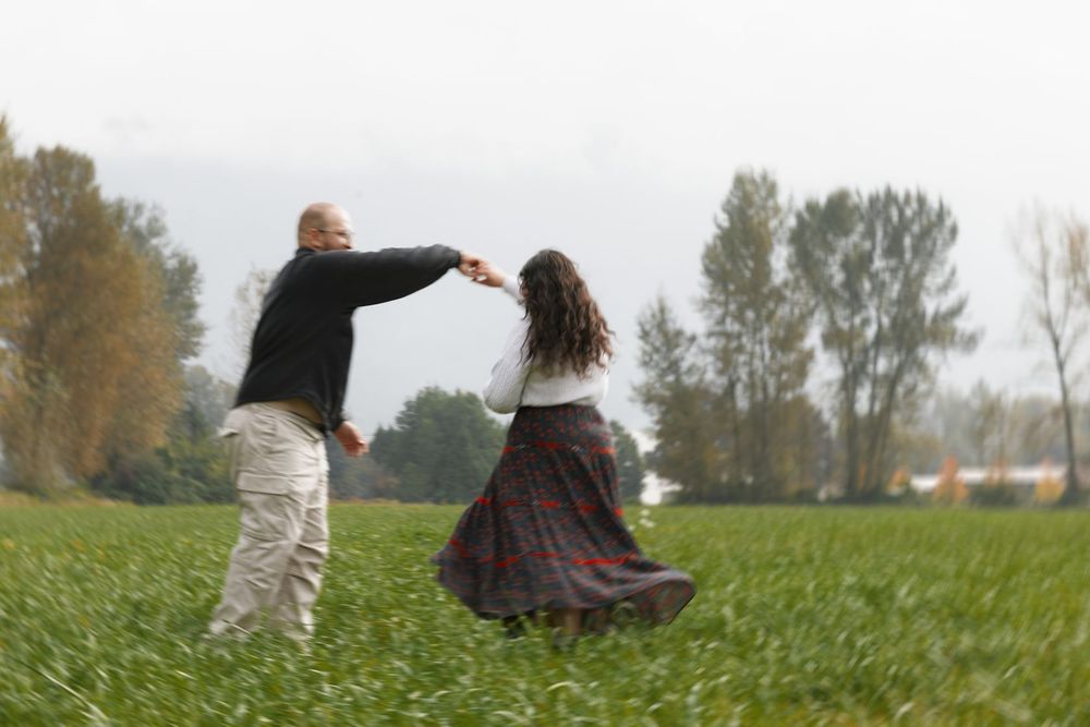 Couple dancing joyfully in a green field with autumn trees in the background.