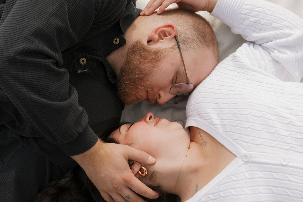 Couple lying down face to face in an intimate moment, man with glasses gently holding woman's head.