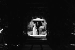 Black and white wedding photo of bride and groom framed in a dark archway with bright garden backdrop.