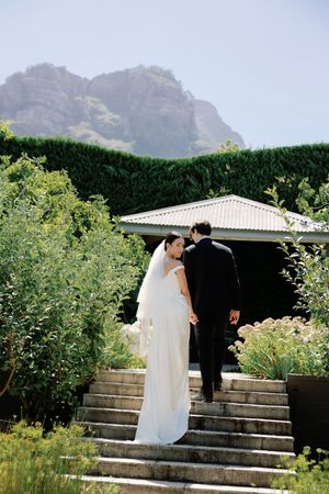Bride and groom walking up stone steps toward a garden pavilion with mountain views on their wedding day.