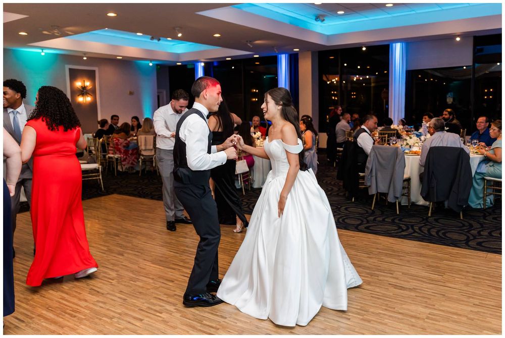 Bride and groom share their first dance on a softly lit dance floor surrounded by wedding guests.