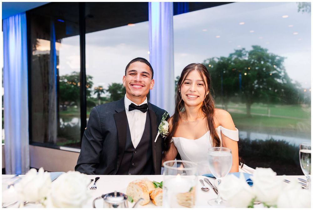 Smiling newlyweds pose together at sweetheart table during their wedding reception dinner.