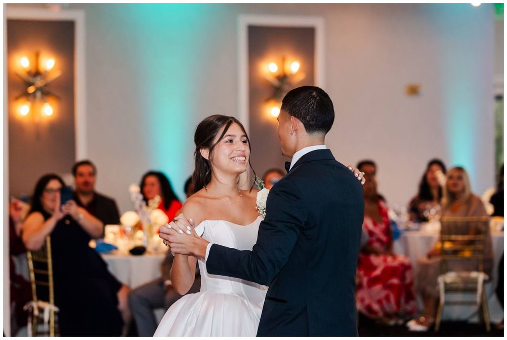 Bride and groom share their first dance at elegant wedding reception with guests watching.