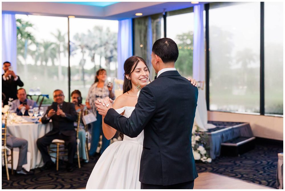 Bride and groom share their first dance at a wedding reception with guests watching in the background.