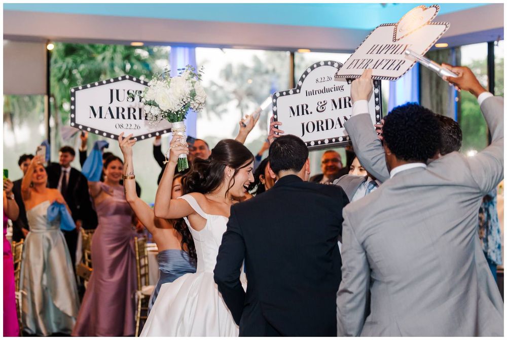 Bride and groom making grand entrance at wedding reception as guests hold Just Married signs.