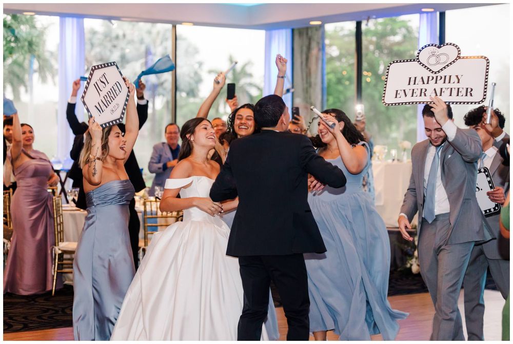 Joyful bride and groom celebrate with wedding party holding happily ever after signs on the dance floor.