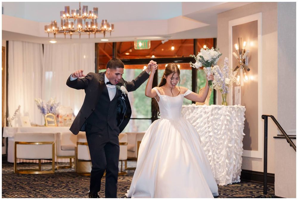 Bride and groom make grand entrance at elegant wedding reception, dancing joyfully under chandelier lighting.