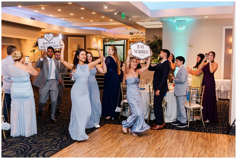 Wedding party celebrating at reception, holding just married signs while dancing in elegant ballroom venue.