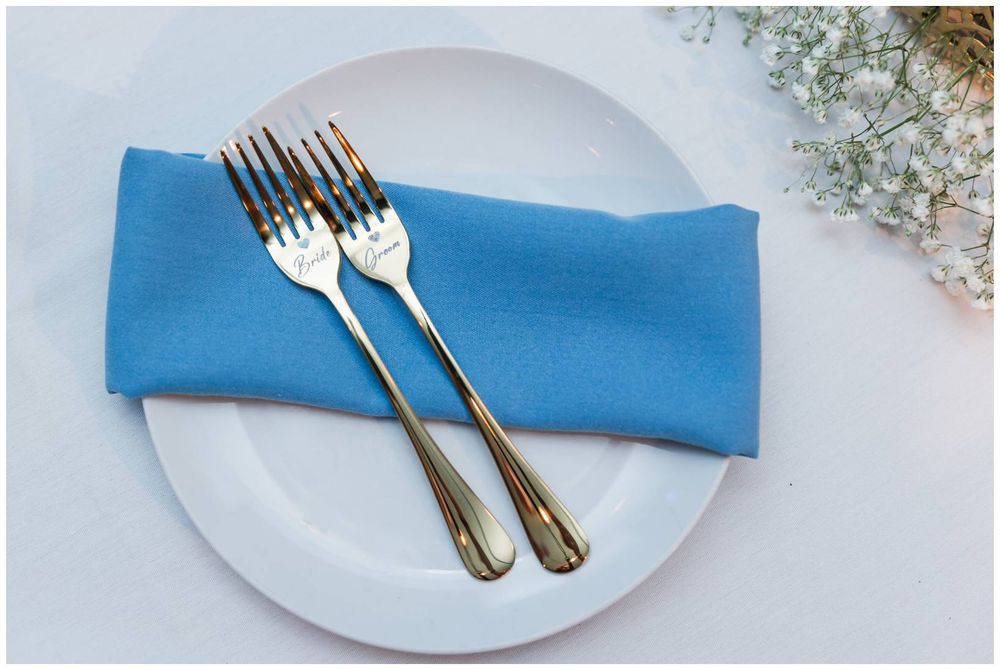 Two engraved silver forks resting on a blue napkin on a white plate, with baby's breath flowers nearby.