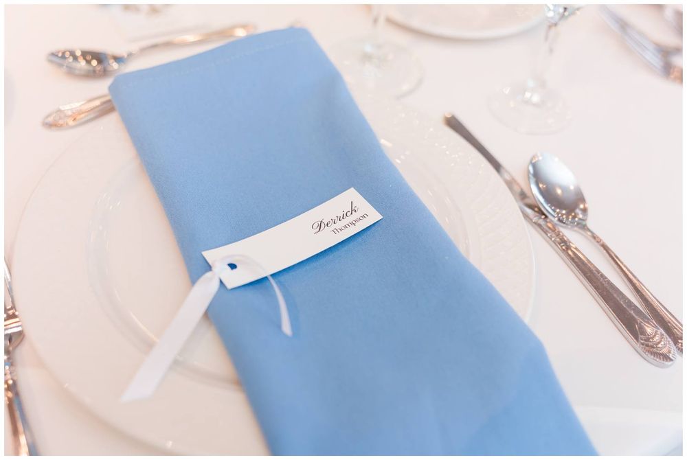 Elegant blue folded napkin with a personalized place card on a formal white wedding reception table setting.