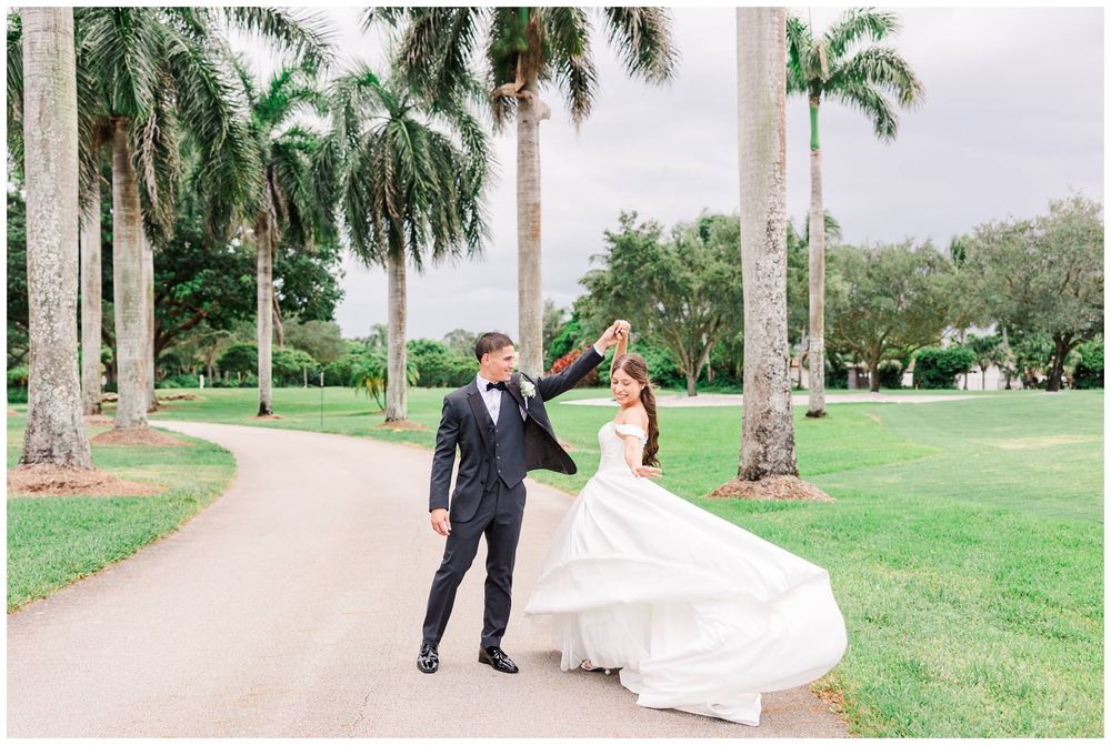 Bride and groom dancing on a palm-lined path at an elegant outdoor wedding venue with lush green lawns.