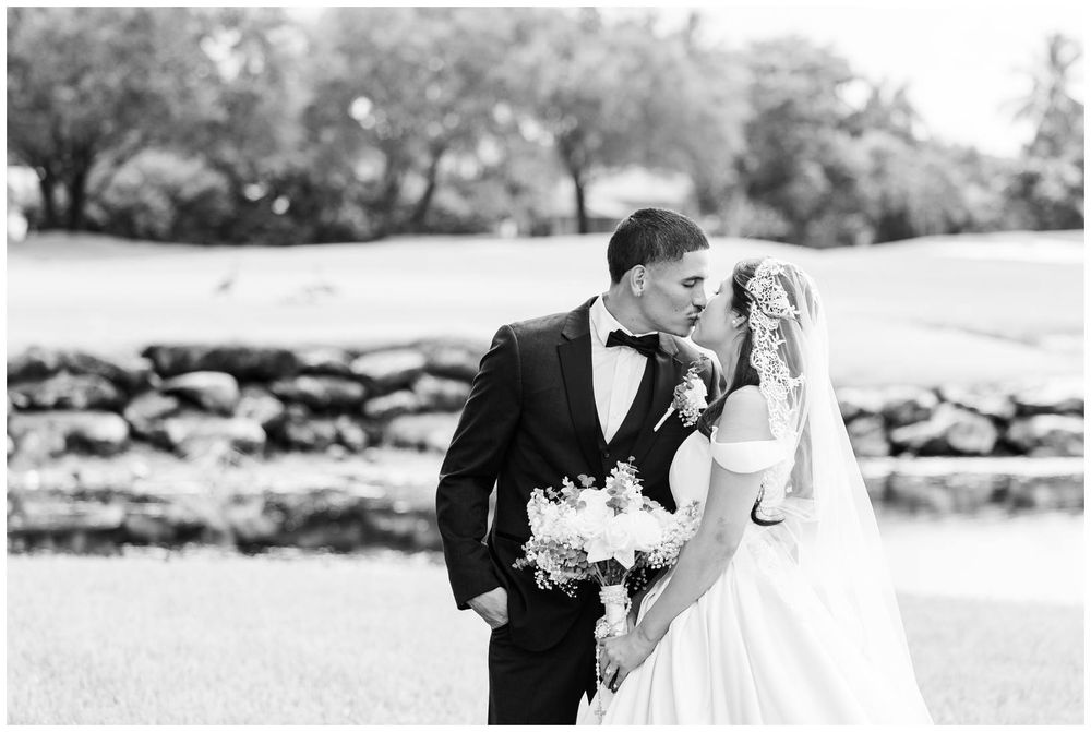 Black and white photo of bride and groom sharing a romantic moment outdoors near a stone wall.