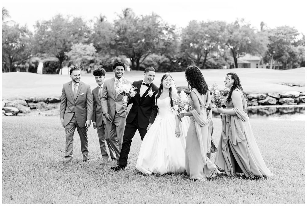 Bride and groom walking joyfully with wedding party in black and white outdoor photo.