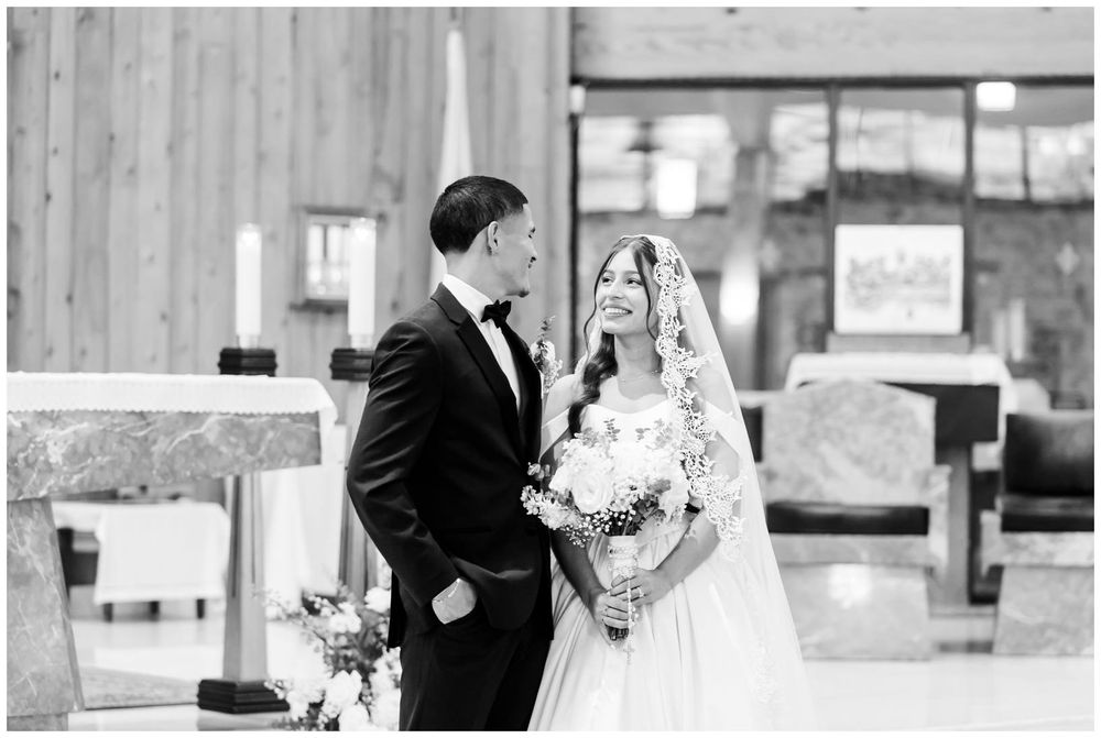 Black and white photo of a bride and groom sharing a joyful moment at the altar during their church wedding ceremony.