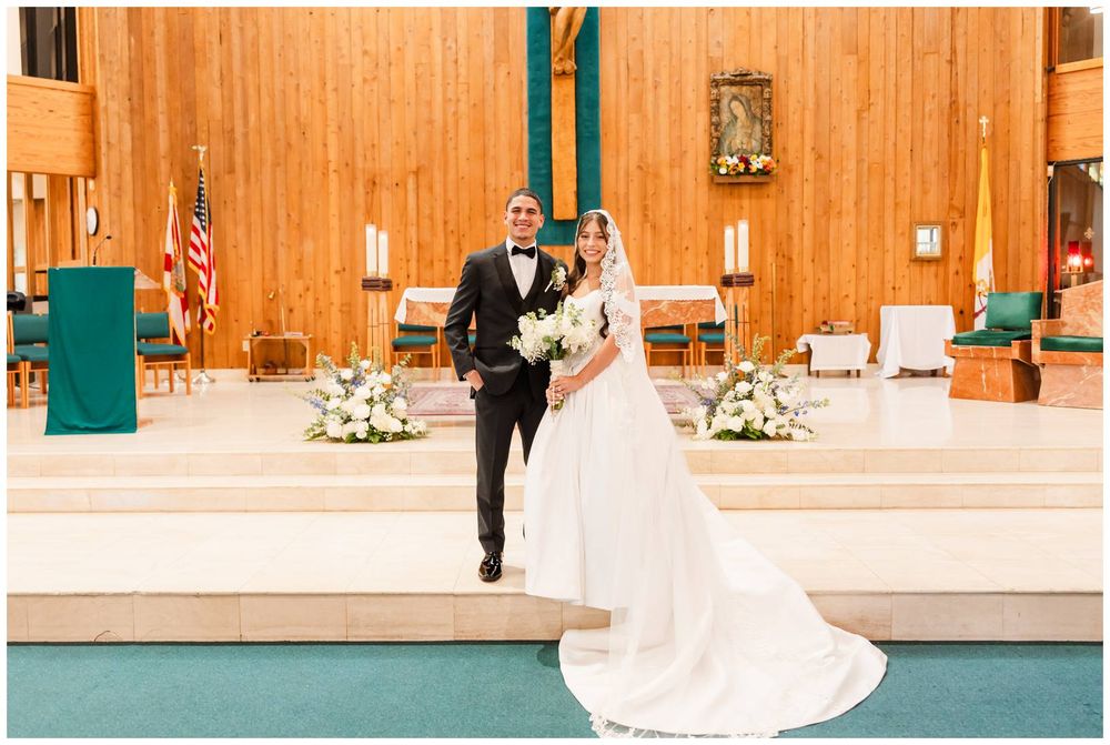Newlyweds walk down the aisle of a Catholic church, bride in a flowing white gown with long train.