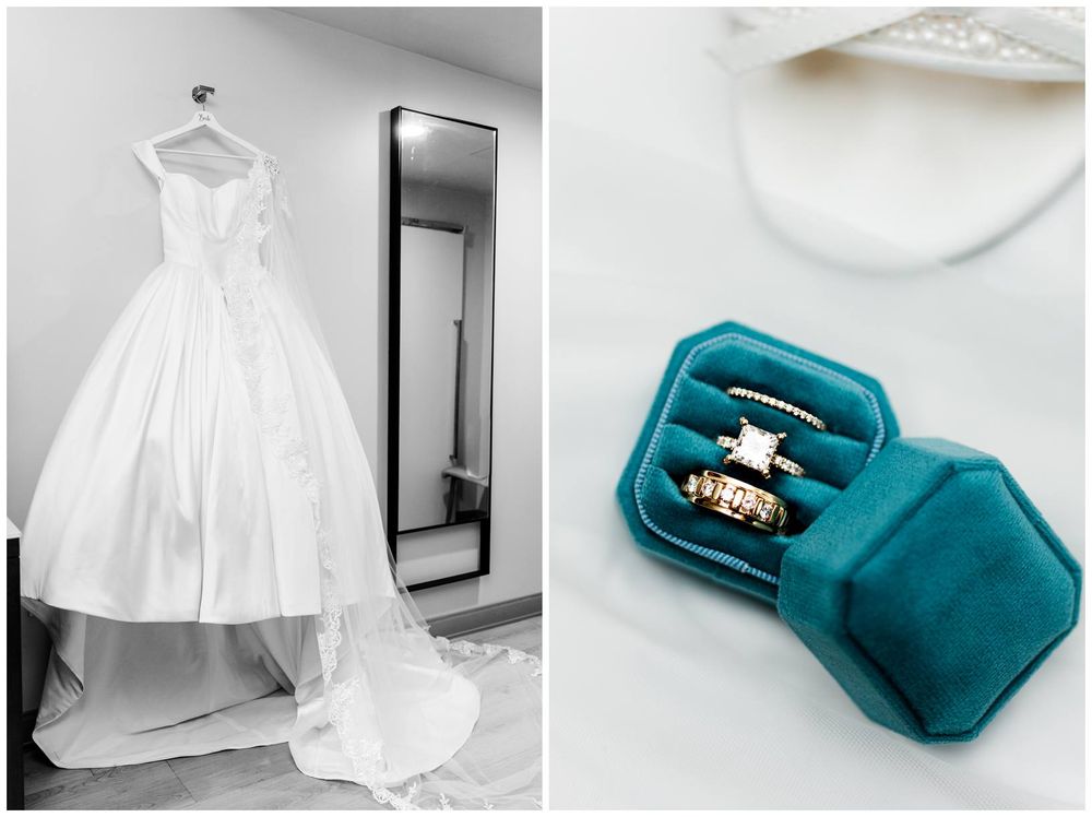 Elegant white ballgown wedding dress hanging near a mirror beside a teal velvet ring box with gold wedding bands.
