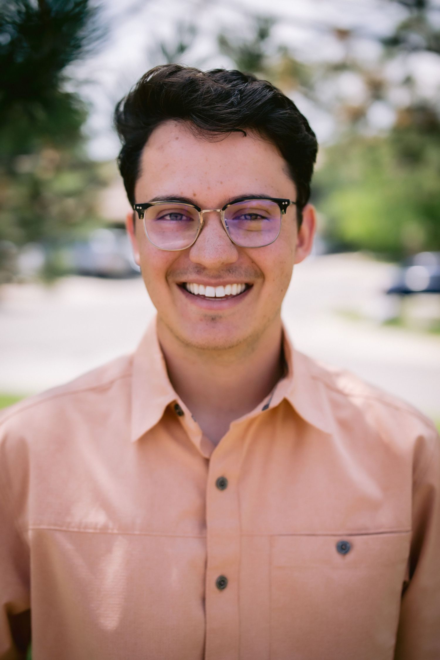 Close-up portrait series of a person in a peach colored shirt smiling warmly while wearing glasses.