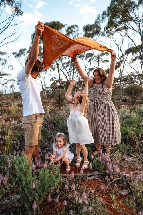 Family playing with orange scarf in Australian bush landscape with purple wildflowers.
