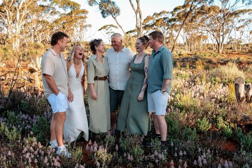 Happy family group laughing together outdoors among wildflowers in an Australian bush landscape at golden hour.