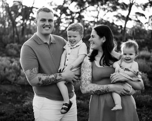Black and white photo of a couple holding two young children outdoors among trees.