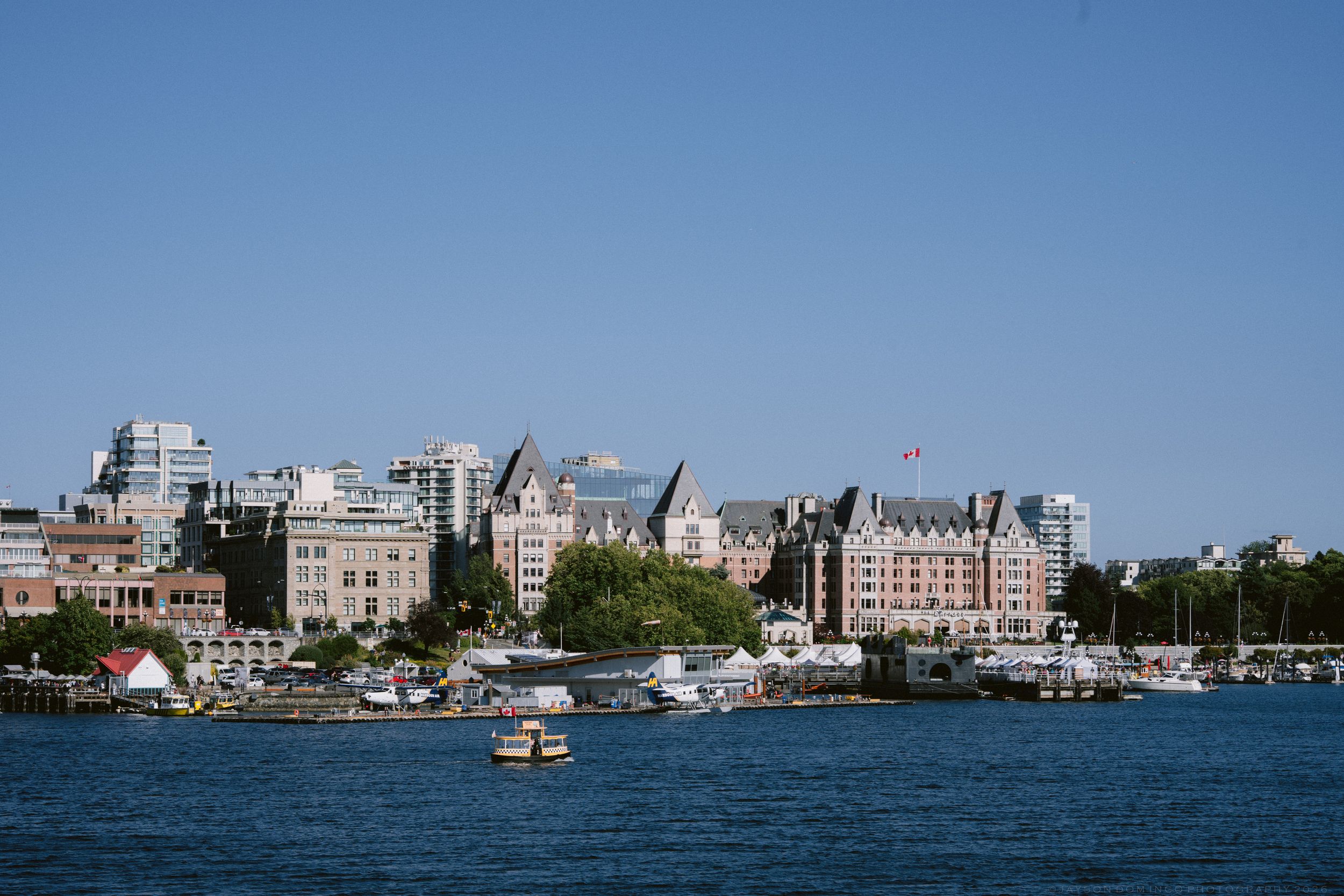 Victoria BC inner harbor skyline with boats on blue water under clear sky.