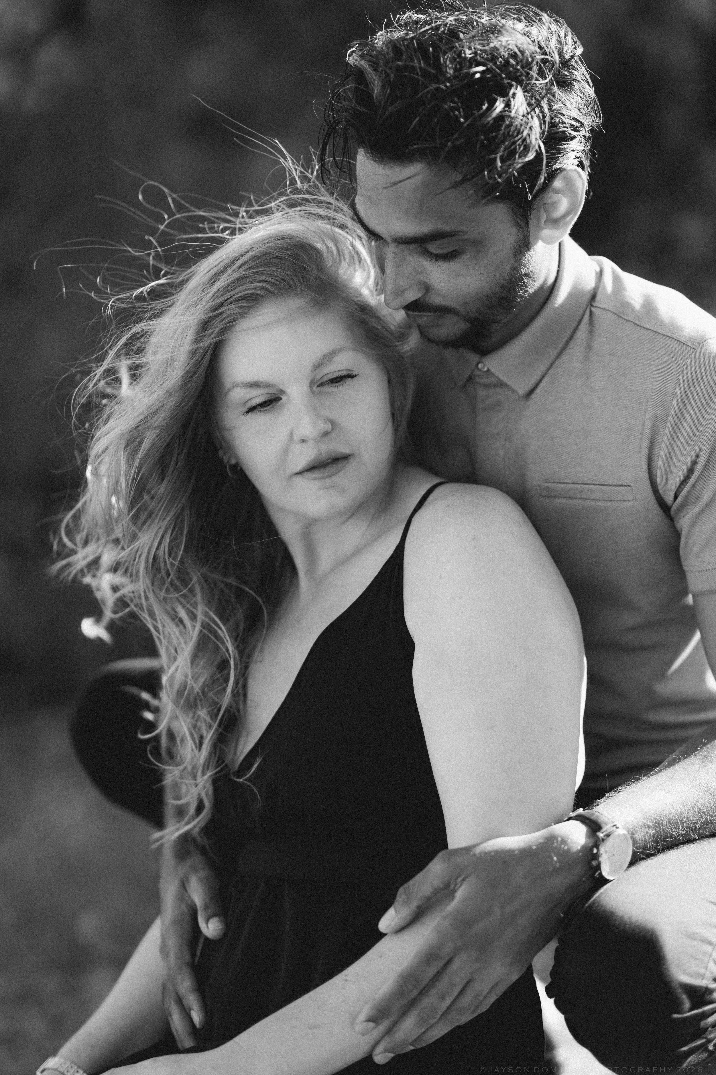 Black and white portrait of couple embracing intimately with wind blowing woman's hair.