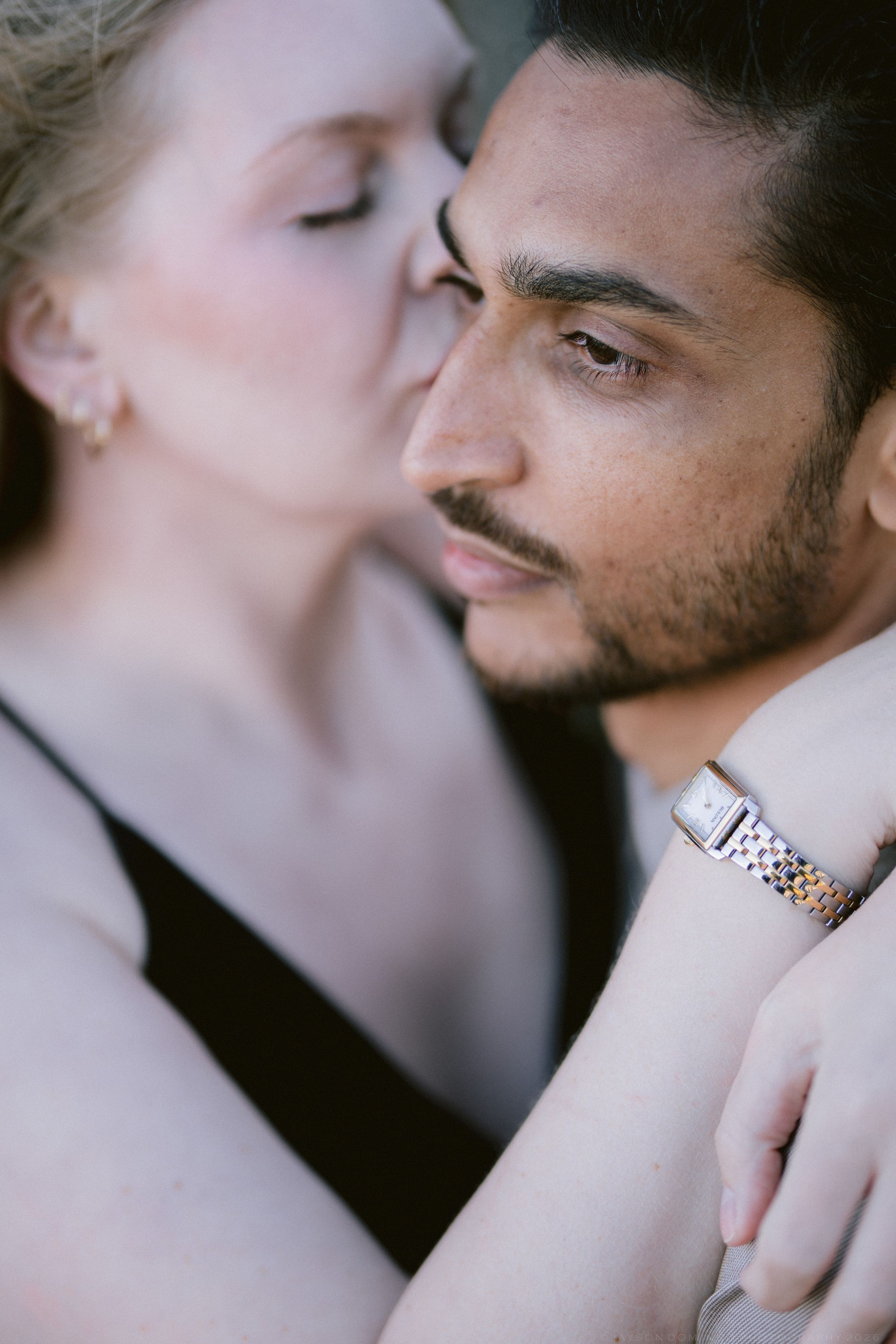 Intimate close-up of interracial couple, woman kissing mans cheek while embracing outdoors.