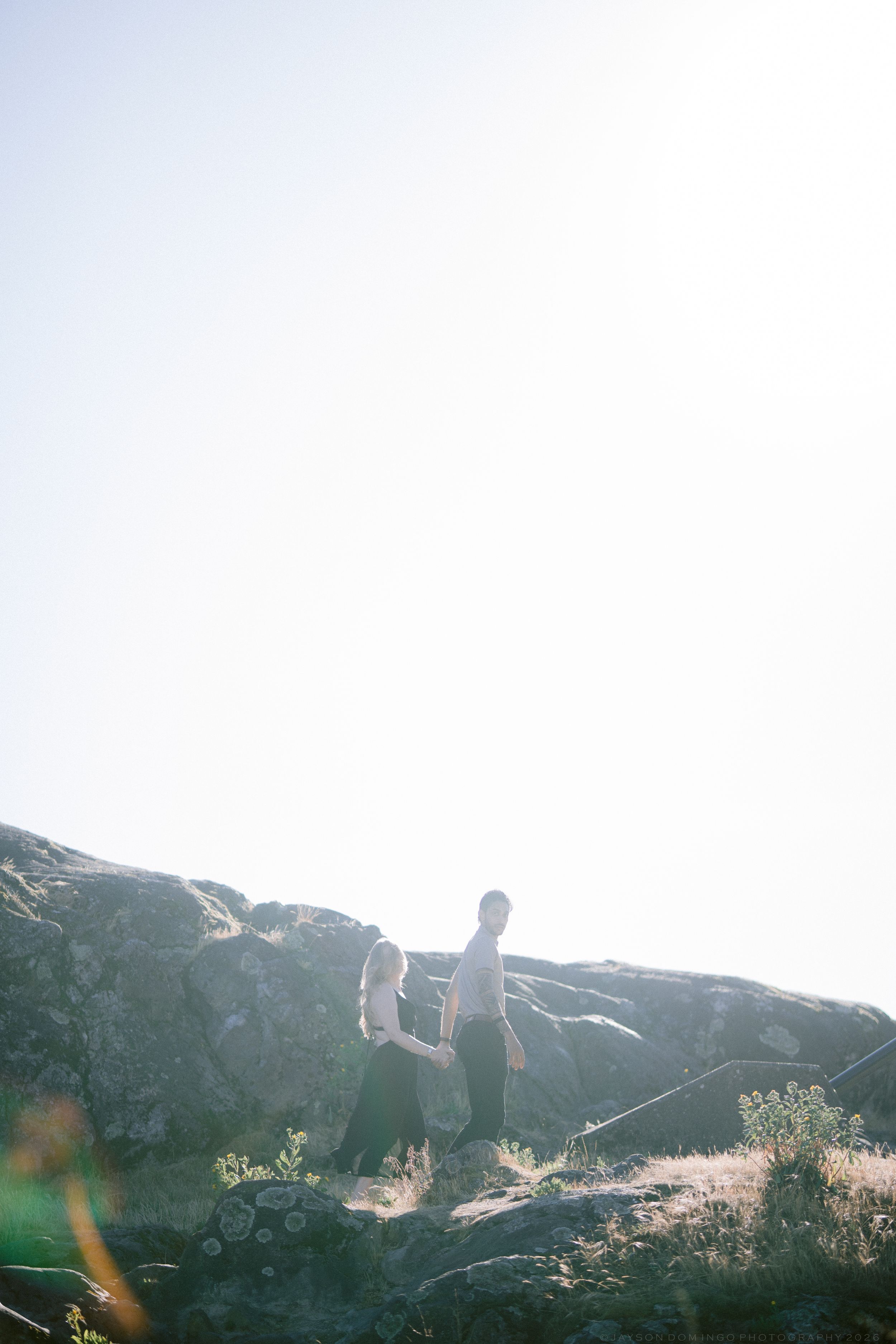 Couple walking among rocky terrain in bright sunlight during an outdoor engagement session.