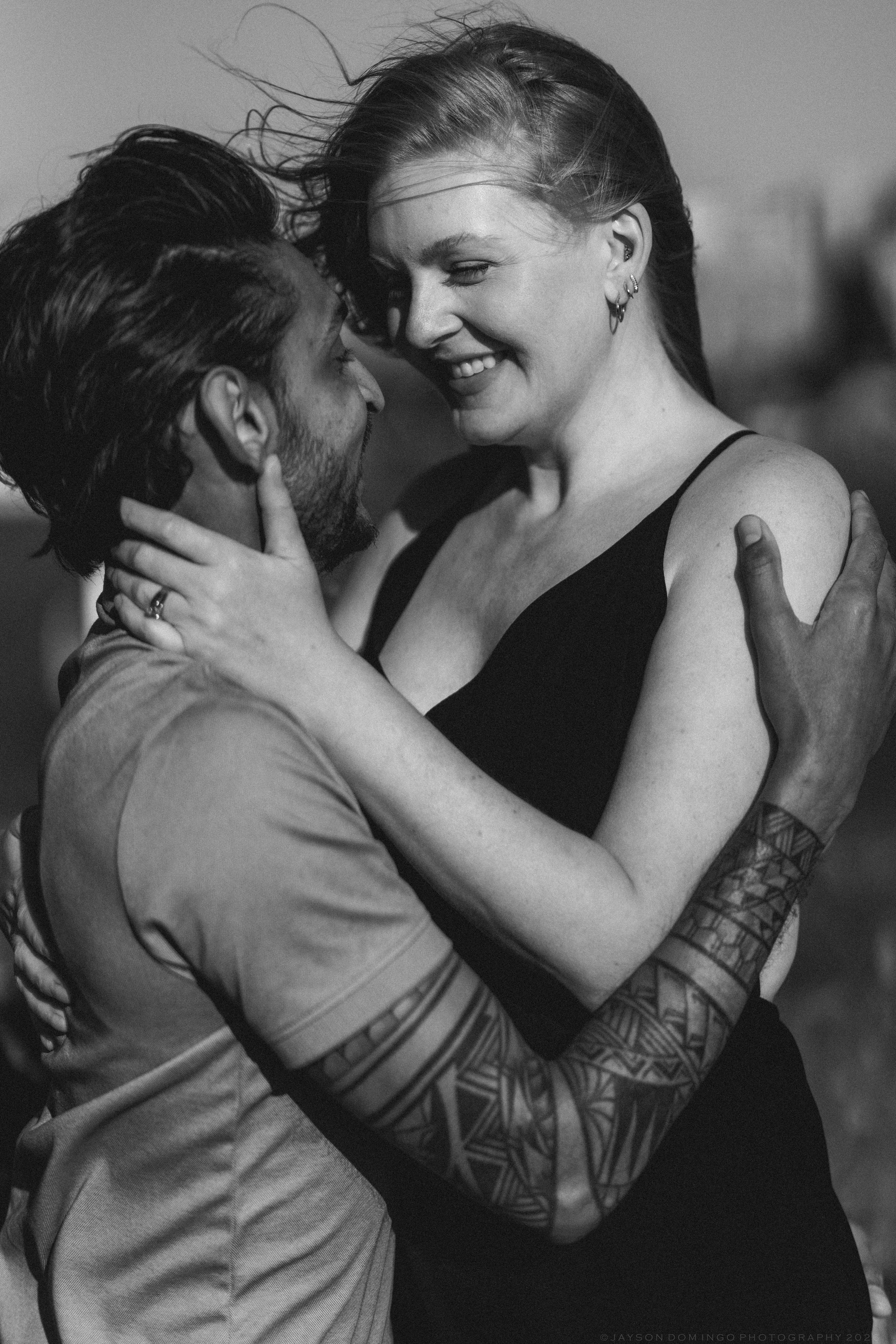 Black and white photo of tattooed couple embracing and smiling outdoors.