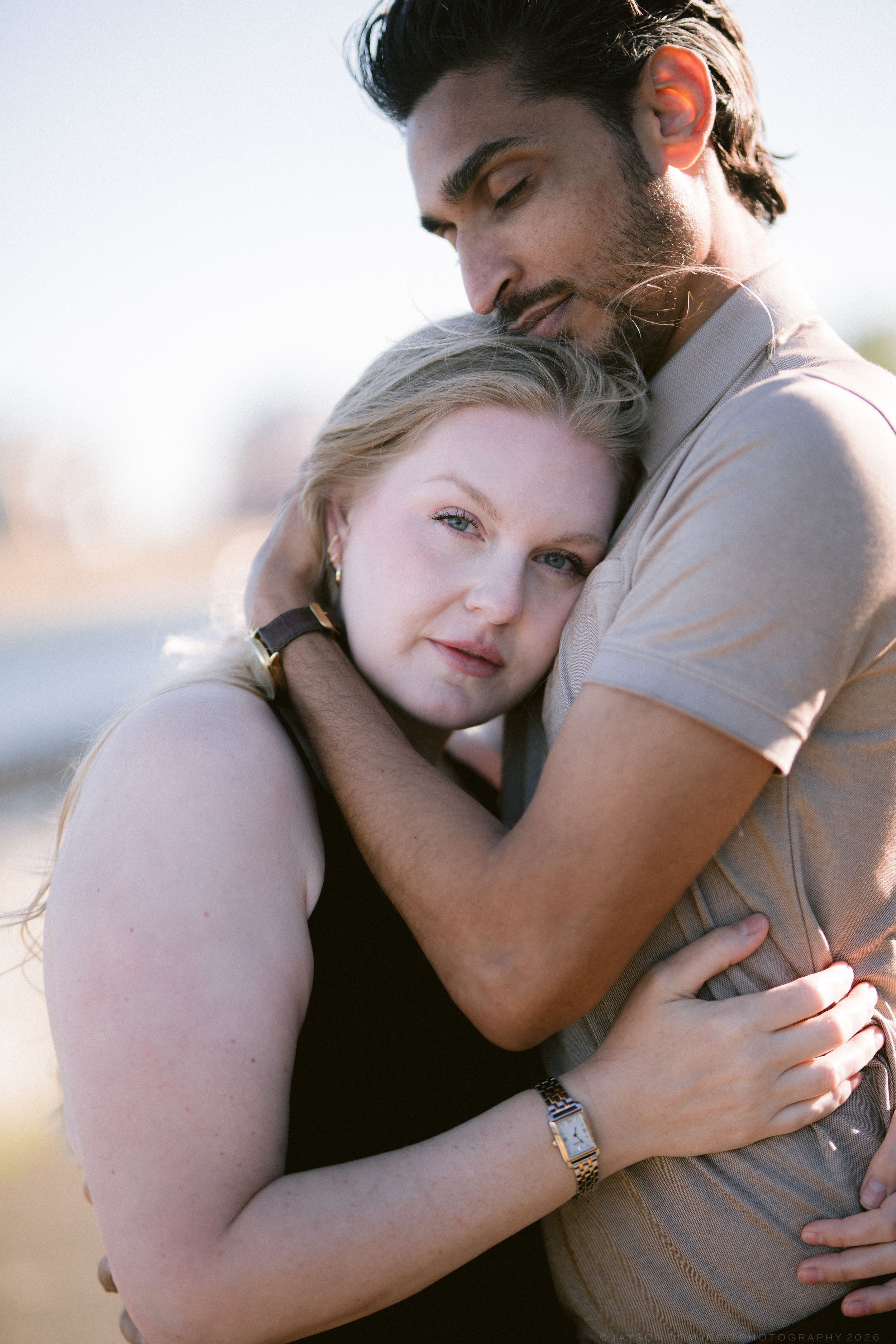 Blonde woman resting her head on a tattooed mans chest as he embraces her outdoors.