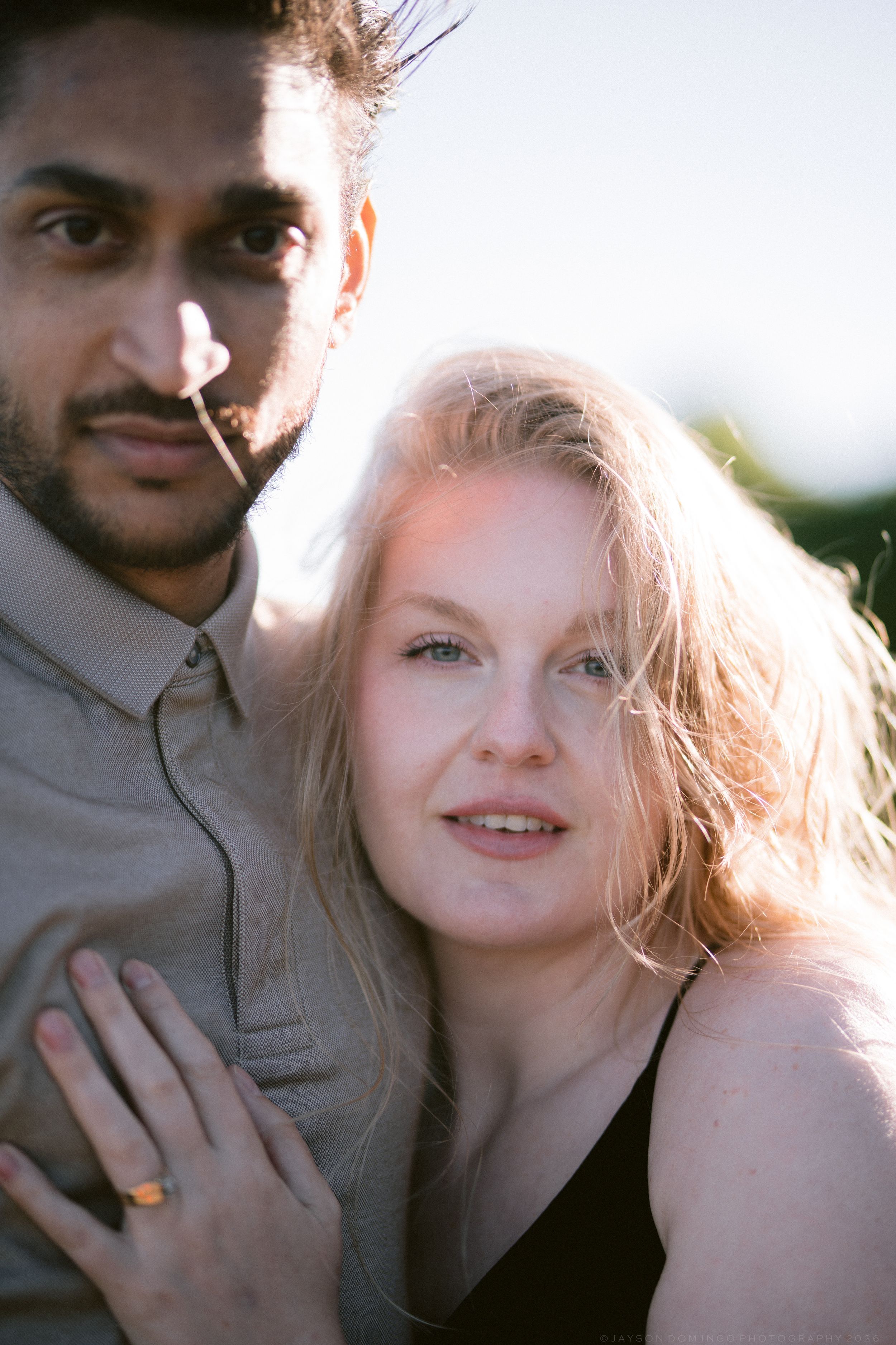 Close-up portrait of smiling blonde woman leaning against tattooed man outdoors.