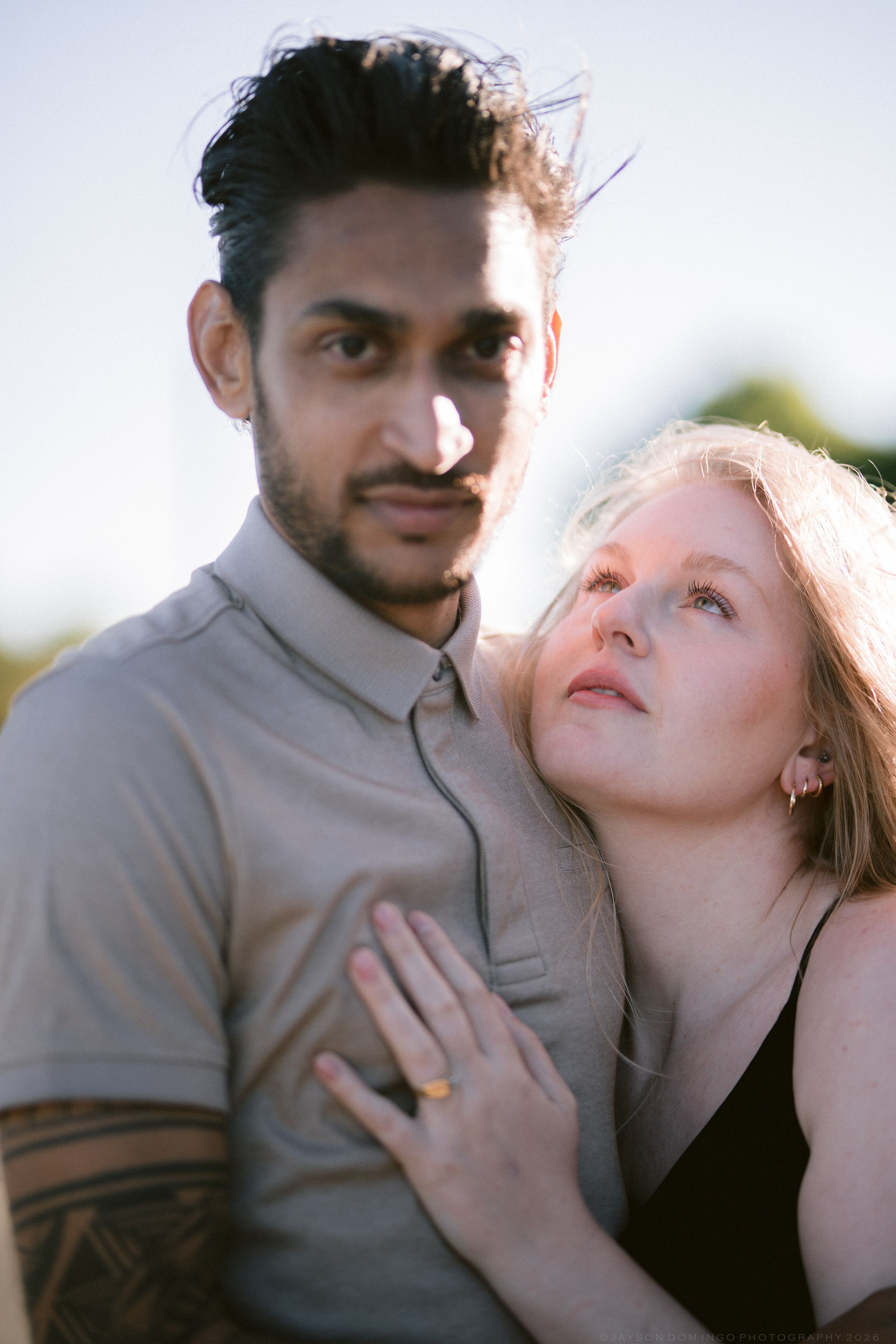 Close portrait of interracial couple outdoors, woman leaning on tattooed mans chest at sunset.