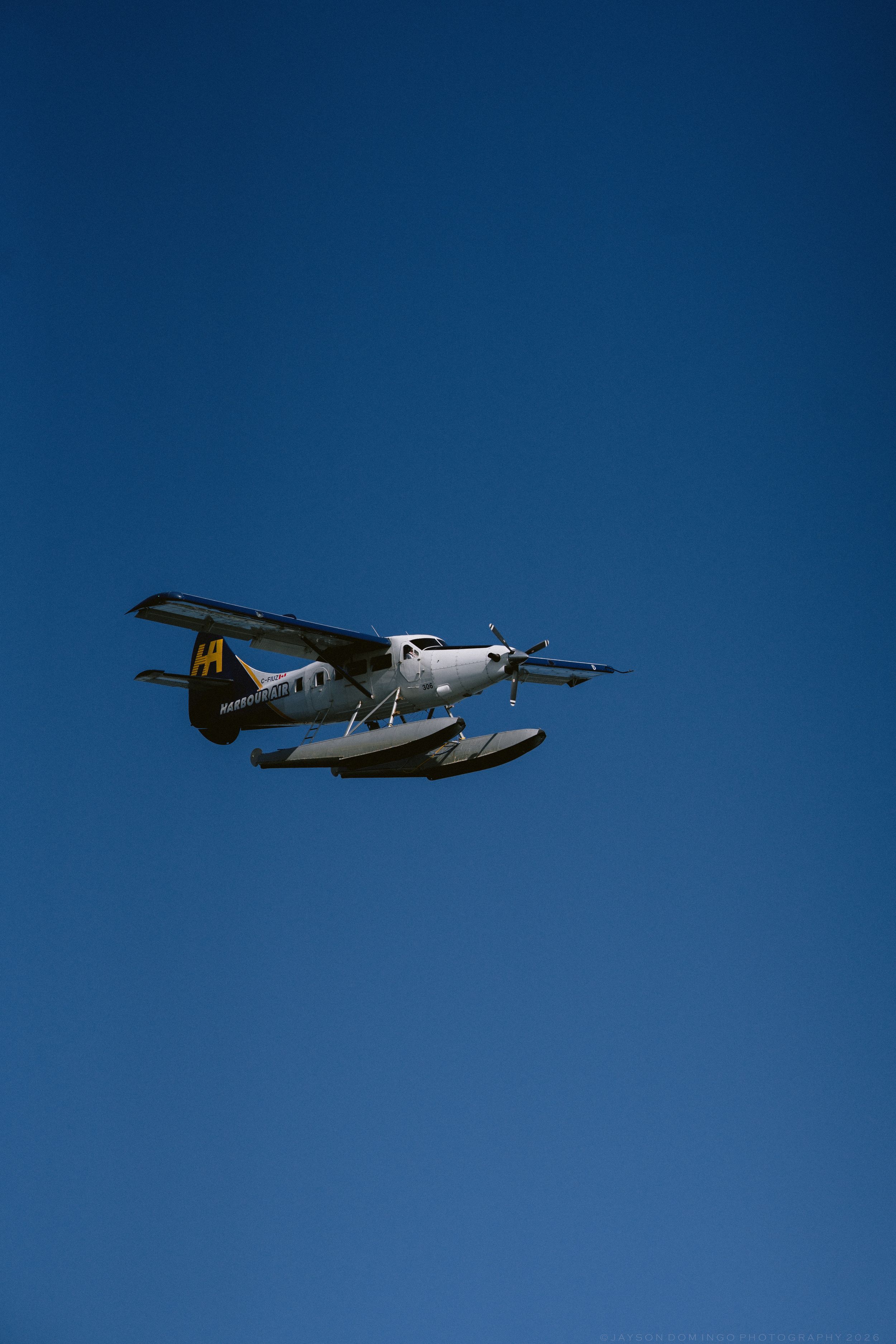 Seaplane with floats flying against a clear blue sky on a sunny day.