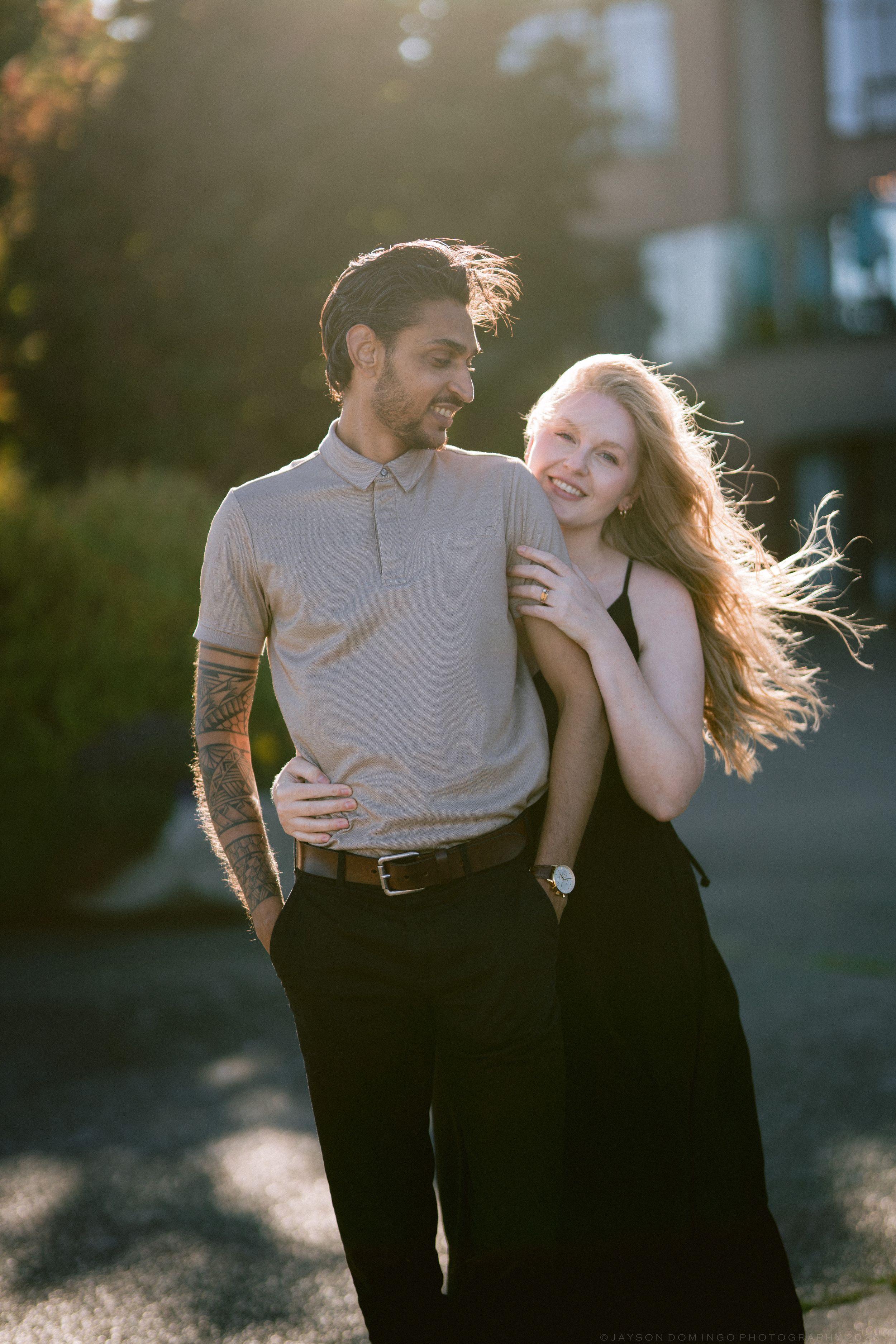 Couple laughing together outdoors in golden hour light, man with tattoos and woman with long blonde hair.